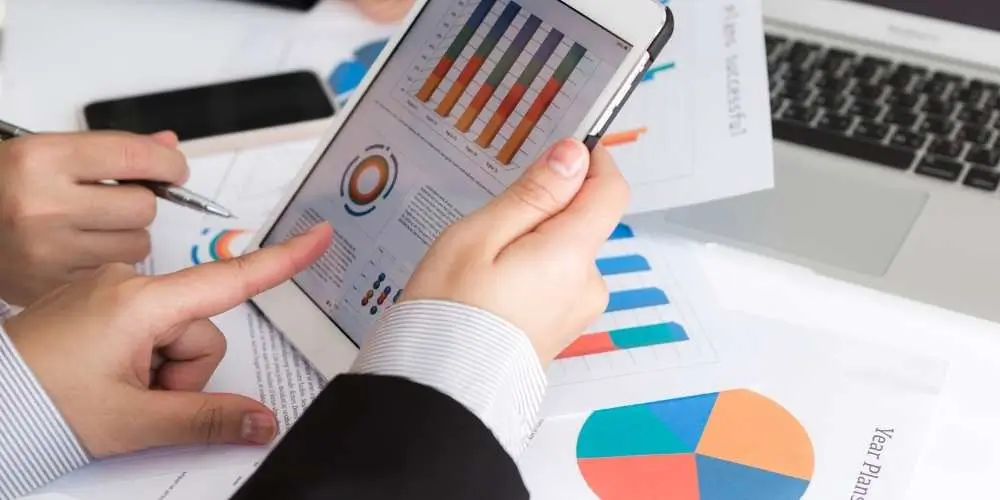 Business professionals analyzing charts and graphs on a tablet and documents, showing bar graphs and pie charts with performance data.