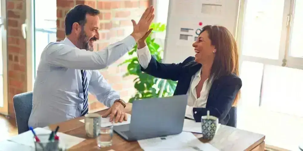 Two business professionals celebrating a successful achievement with a high-five, symbolizing partnership and success in the workplace.