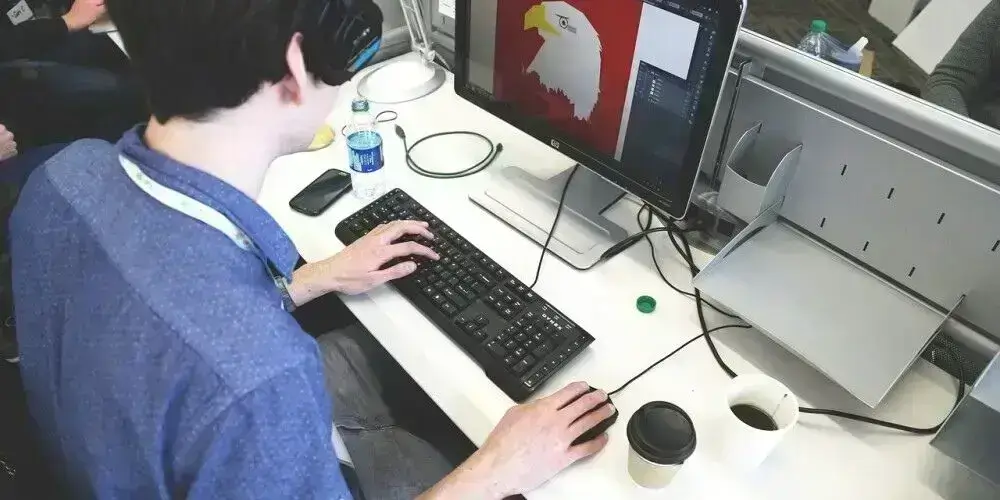 A person working on graphic design software at a desktop computer, creating an illustration of an eagle.