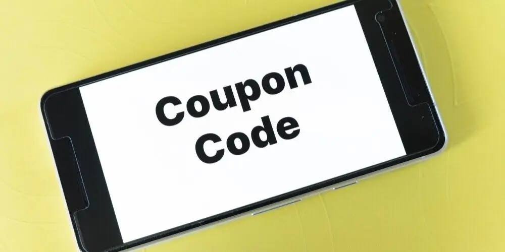 A smartphone displaying the words "Coupon Code" on its screen, placed on a light yellow background.