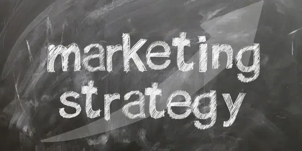 The words "Marketing Strategy" written in chalk on a blackboard with a faint upward arrow in the background.