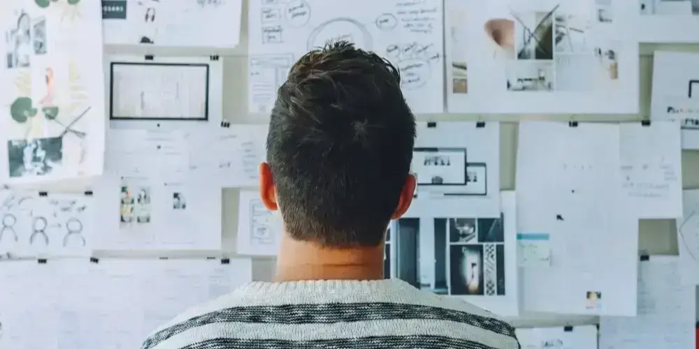 A person facing a wall covered with notes and plans, symbolizing the importance of consistency and structured routines in achieving long-term goals.