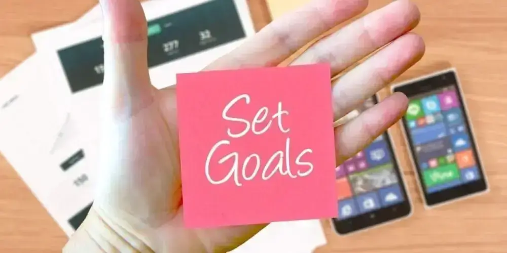 A hand holding a sticky note with "Set Goals" written on it, representing the importance of goal-setting in effective time management.